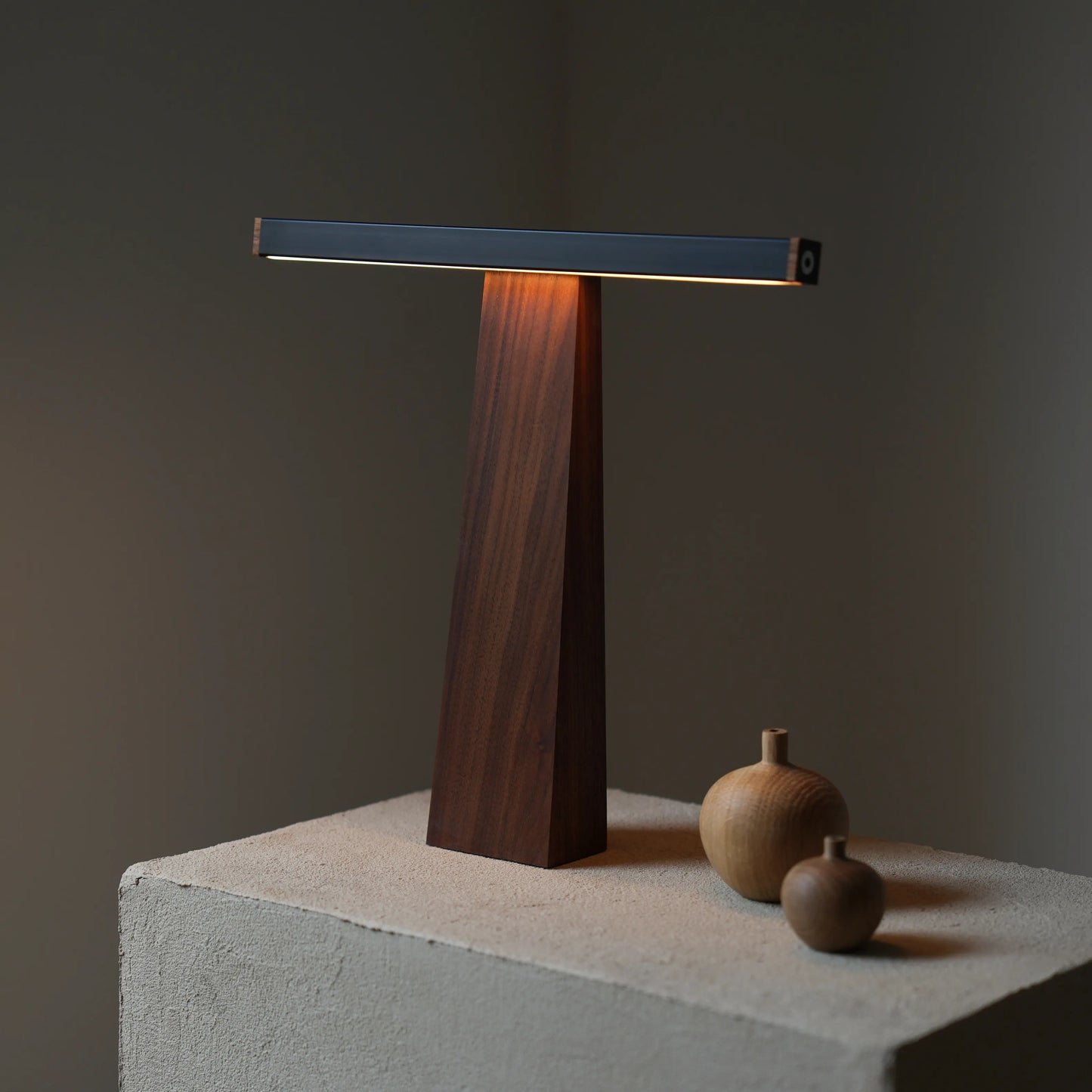 Sculptural LED lamp positioned on a concrete block with small wooden vase.