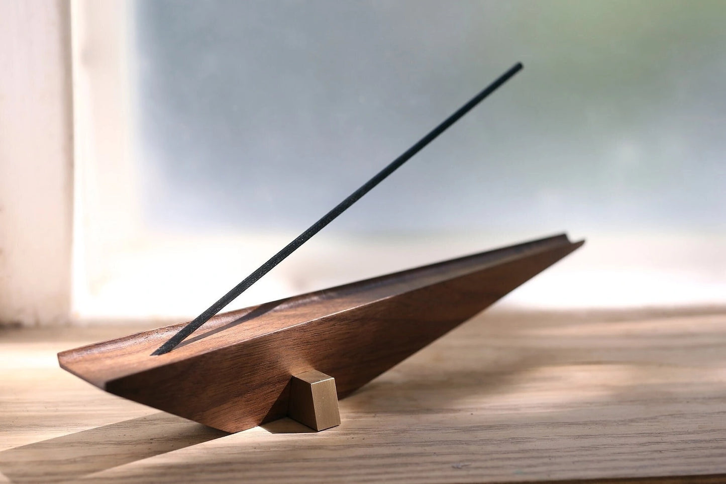 An architectural incense holder styled on a wooden desk near a window.