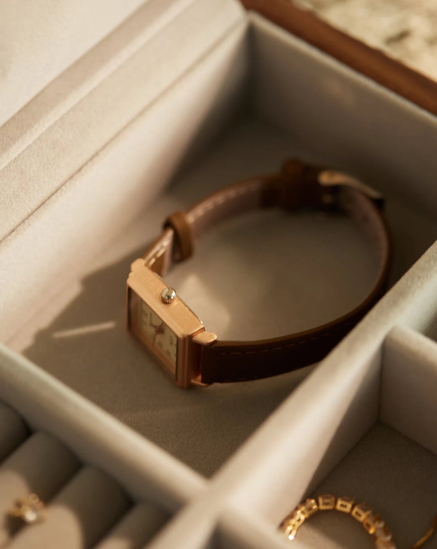 A classic watch sitting inside a compartment of a wood jewelry box.