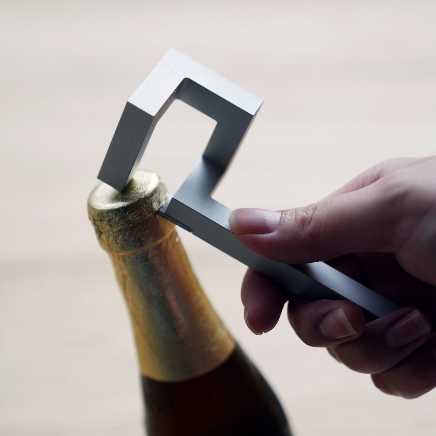 Hand opening a bottle with a silver geometric aluminum opener.