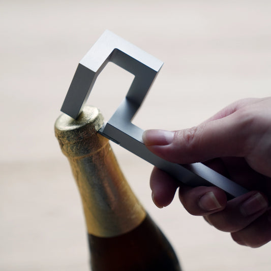 Hand opening a bottle with a silver geometric aluminum opener.