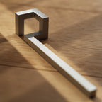 Minimalist silver bottle opener on wood in dramatic sunlight.