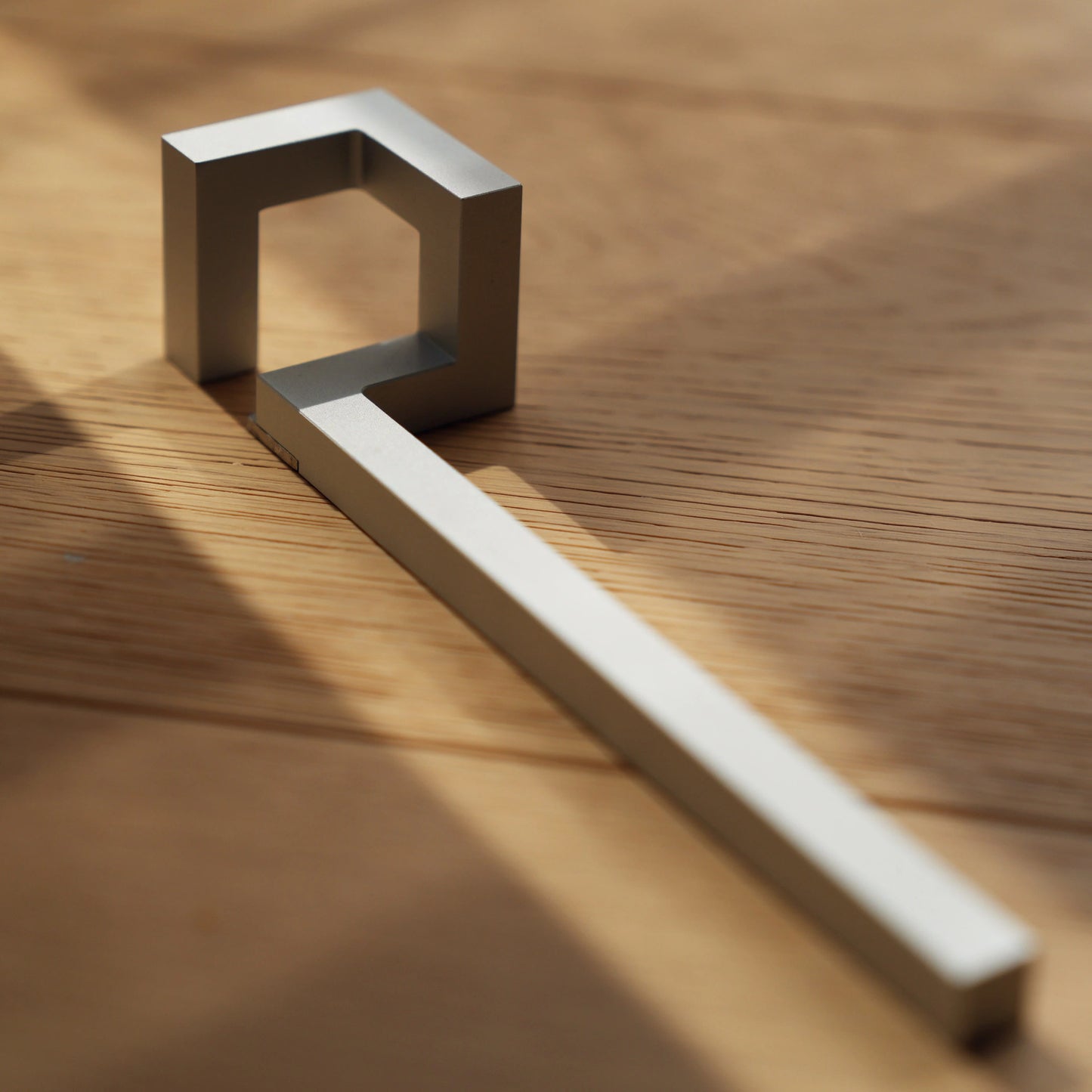 Minimalist silver bottle opener on wood in dramatic sunlight.