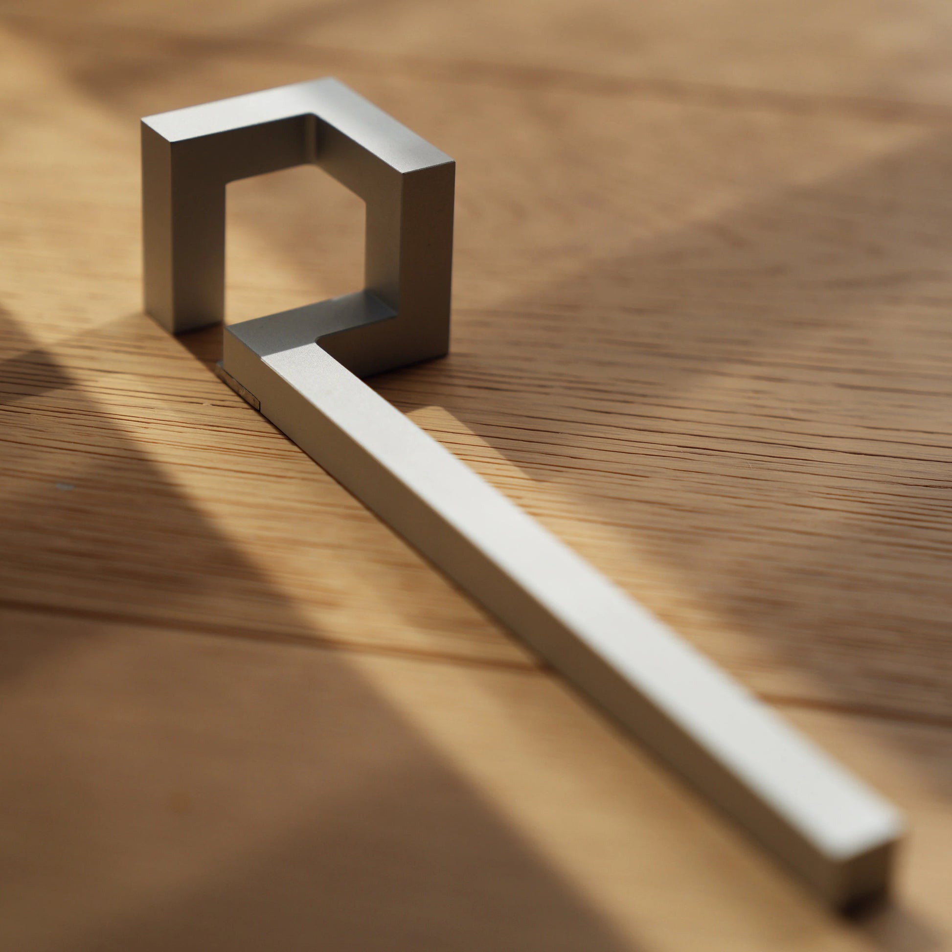 Minimalist silver bottle opener on wood in dramatic sunlight.