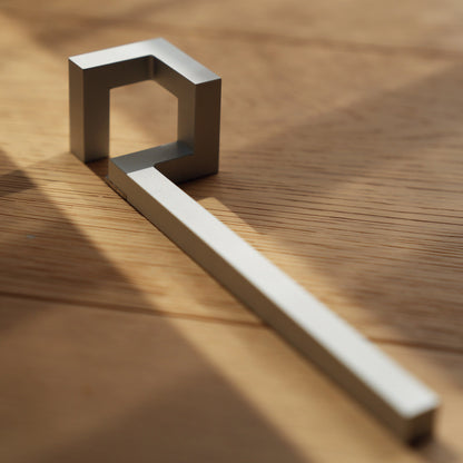 Minimalist silver bottle opener on wood in dramatic sunlight.