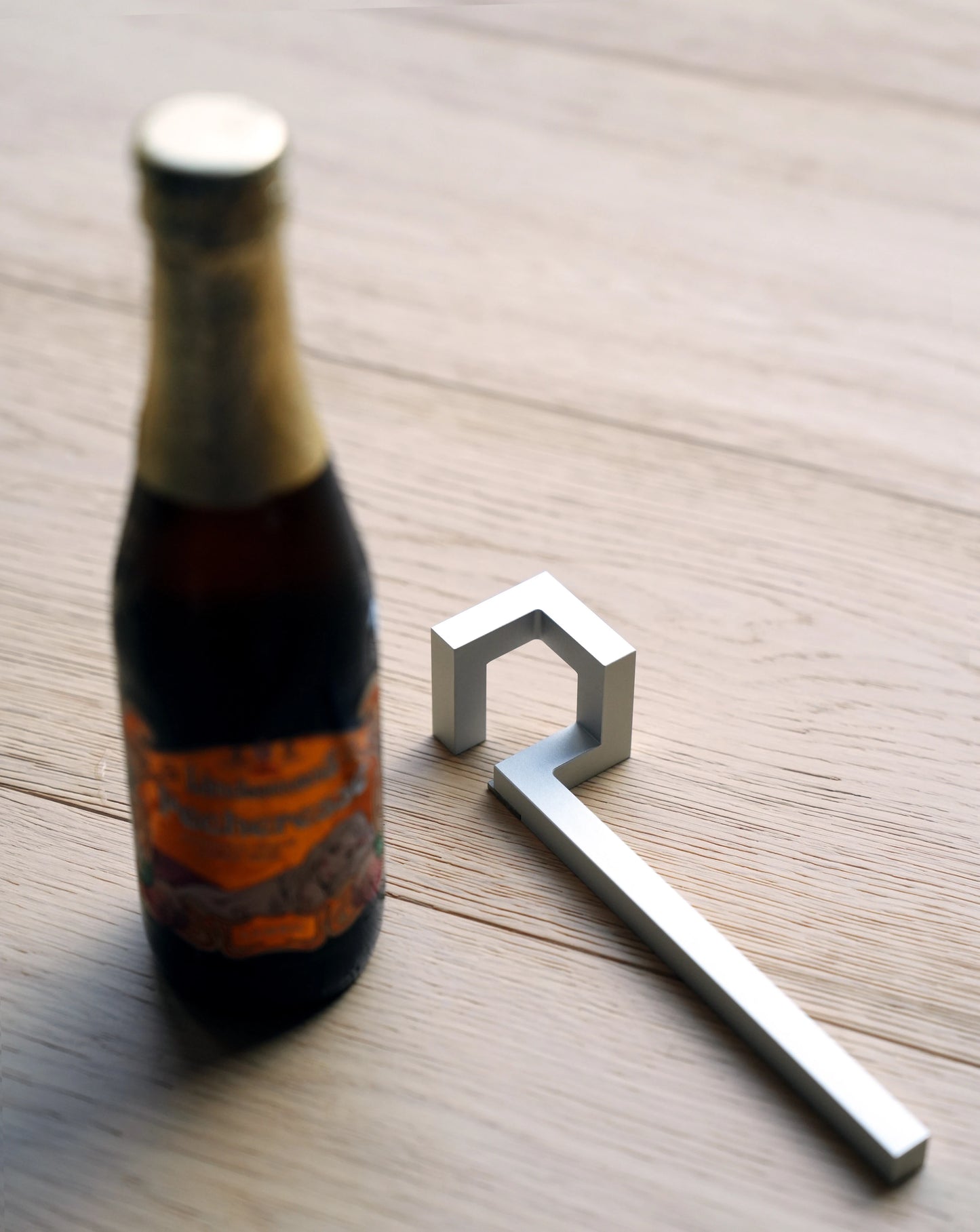 Geometric silver aluminum bottle opener lying next to a beer bottle.