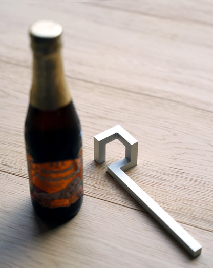 Geometric silver aluminum bottle opener lying next to a beer bottle.