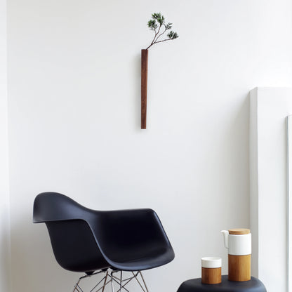 A minimalist walnut wall vase holding a green branch in a modern room.