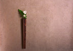 A solid walnut wall vase with a small white flower against a brown wall.