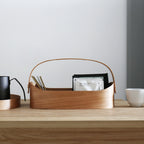 A cherry wood bentwood caddy with tea supplies on a wooden desk.