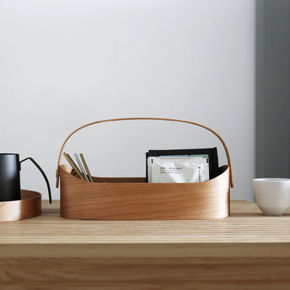 A cherry wood bentwood caddy with tea supplies on a wooden desk.