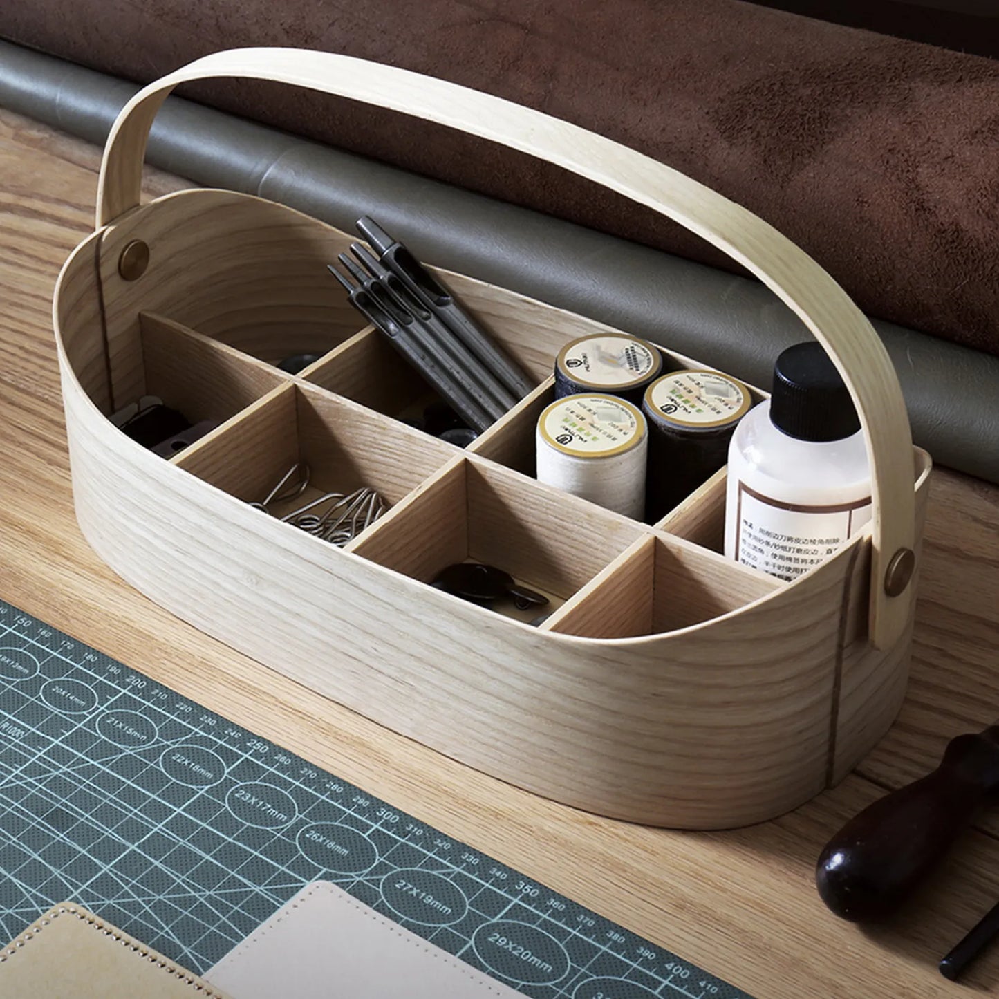 A white wax wood bentwood caddy holding leatherworking craft supplies.