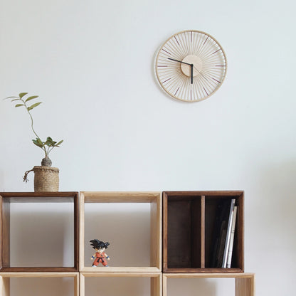 A minimalist bamboo spoke clock on a white wall above modular wood shelving.
