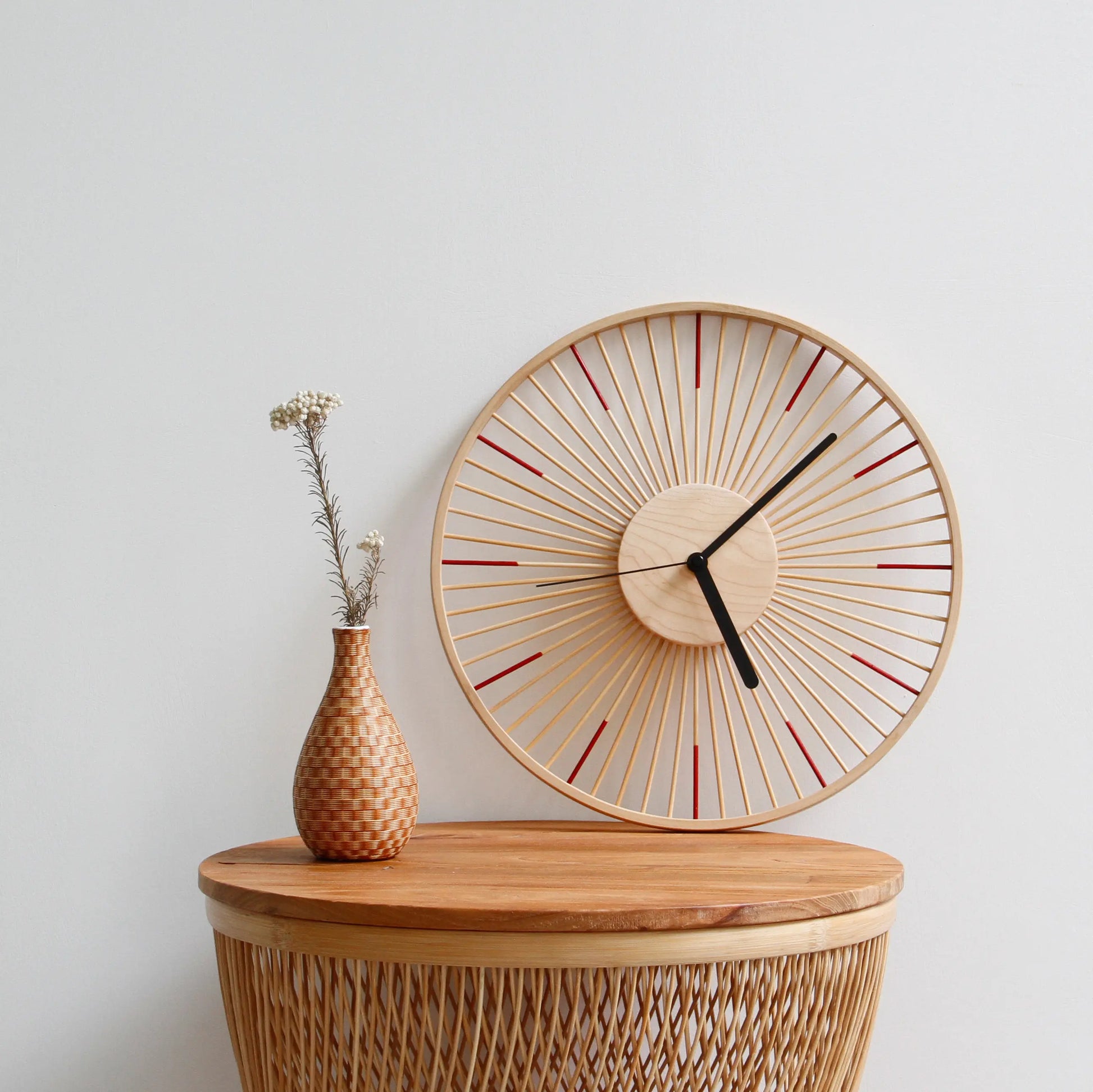 A red-accented bamboo clock on a wicker table with a small vase.