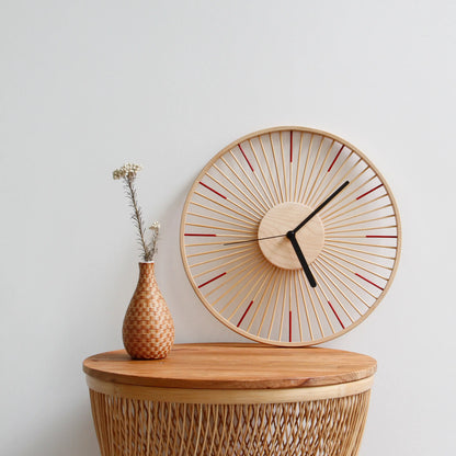 A red-accented bamboo clock on a wicker table with a small vase.