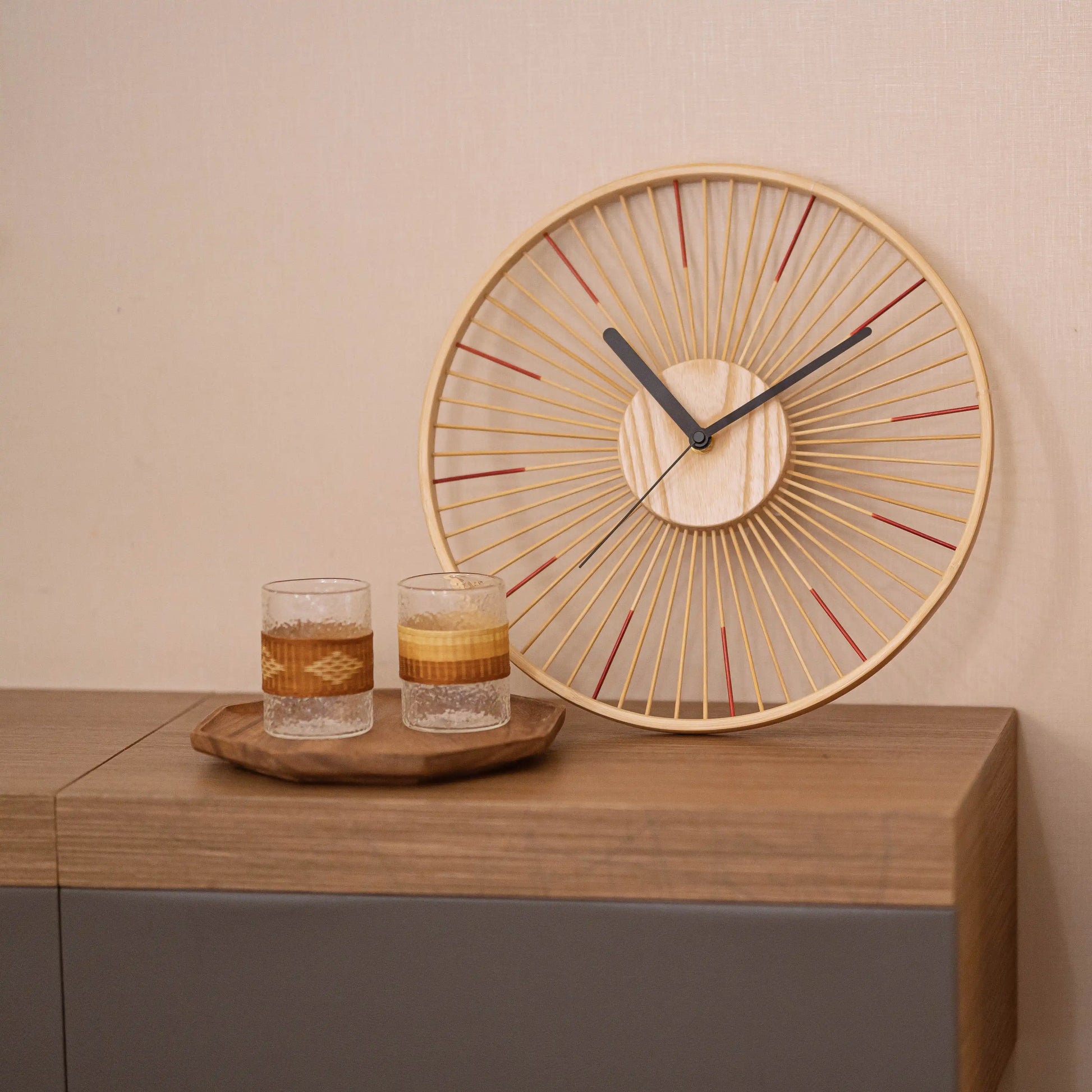 A bamboo spoke clock with red accents sitting on a modern sideboard.
