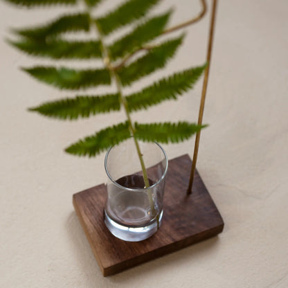 Close-up of a fern stem in the glass cup of a walnut bud vase.