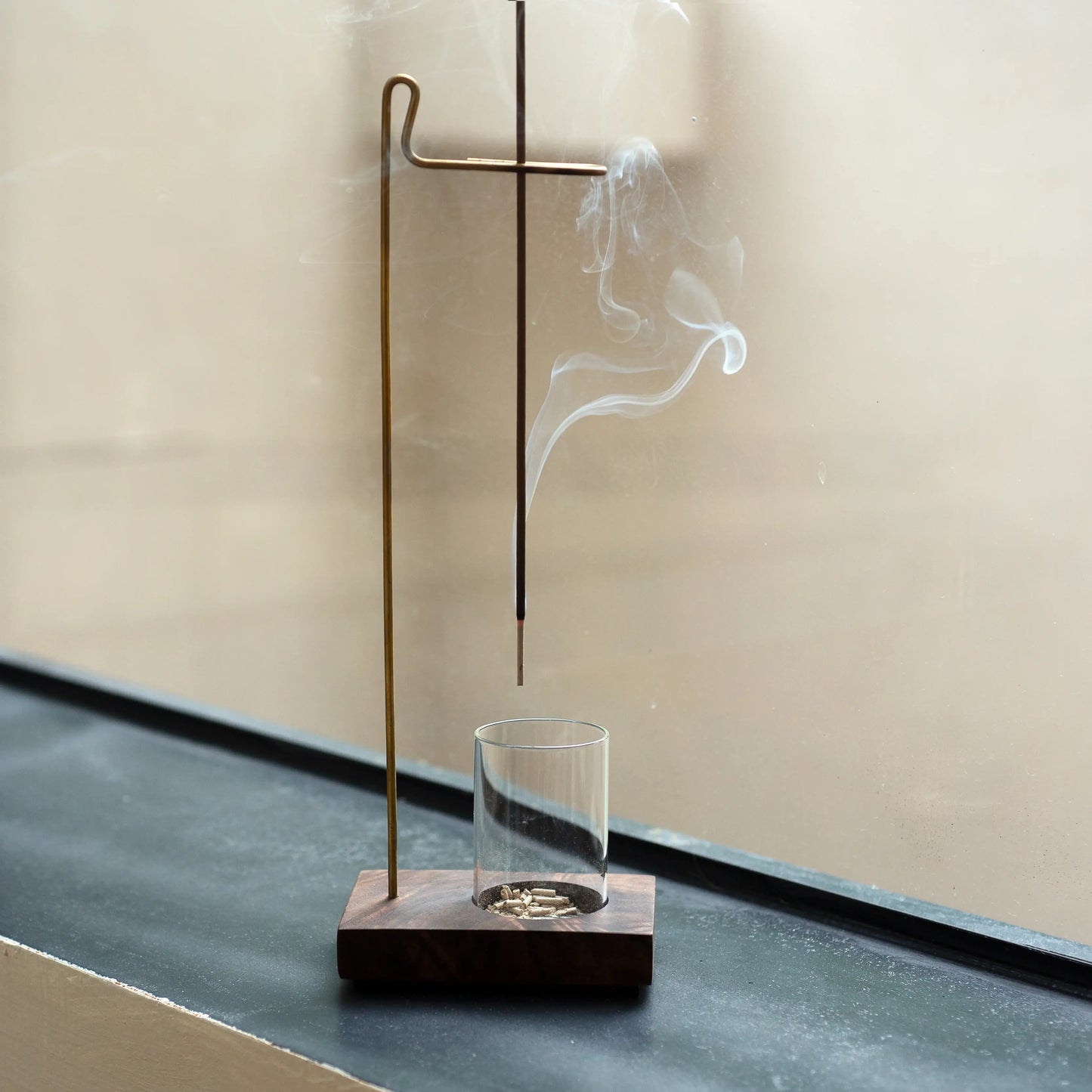 Suspension incense holder with a glass ash catcher on a windowsill.