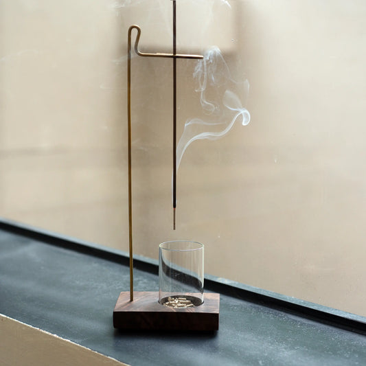 Suspension incense holder with a glass ash catcher on a windowsill.