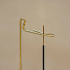 Detailed view of the brass hook holding a thin stick of incense.