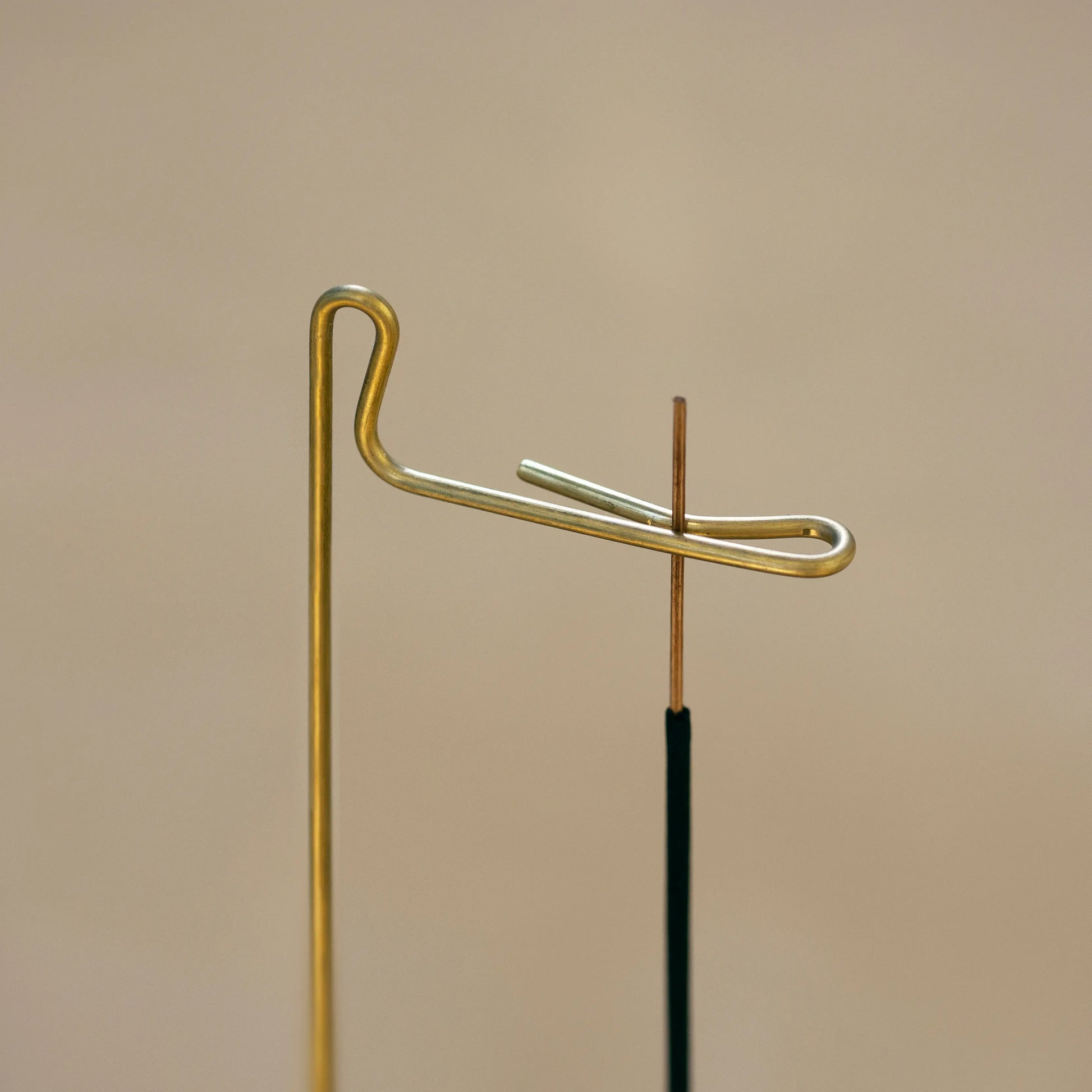Detailed view of the brass hook holding a thin stick of incense.