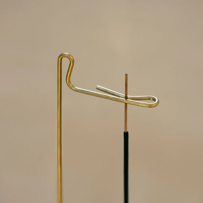 Detailed view of the brass hook holding a thin stick of incense.