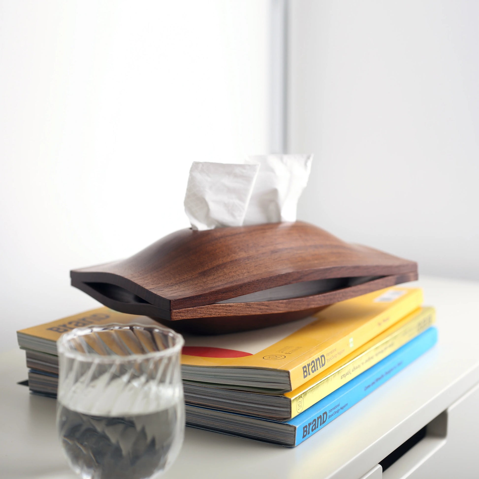 A black walnut wood tissue box styled on a stack of books with a water glass.