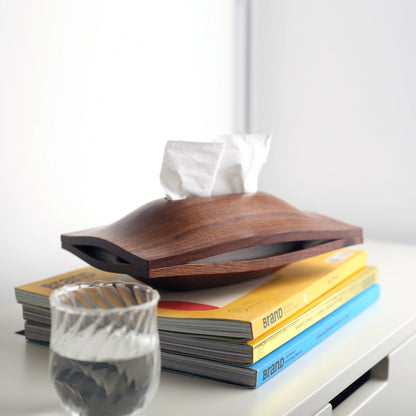 A black walnut wood tissue box styled on a stack of books with a water glass.