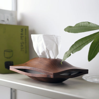 Angled view of the walnut tissue box cover on a shelf with a plant.