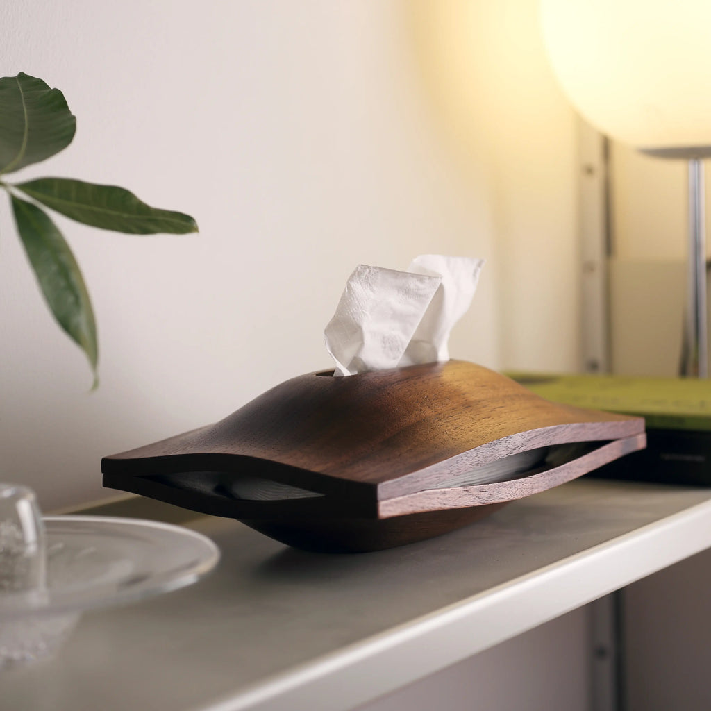 Sculptural wood tissue holder on a shelf under the warm glow of a lamp.