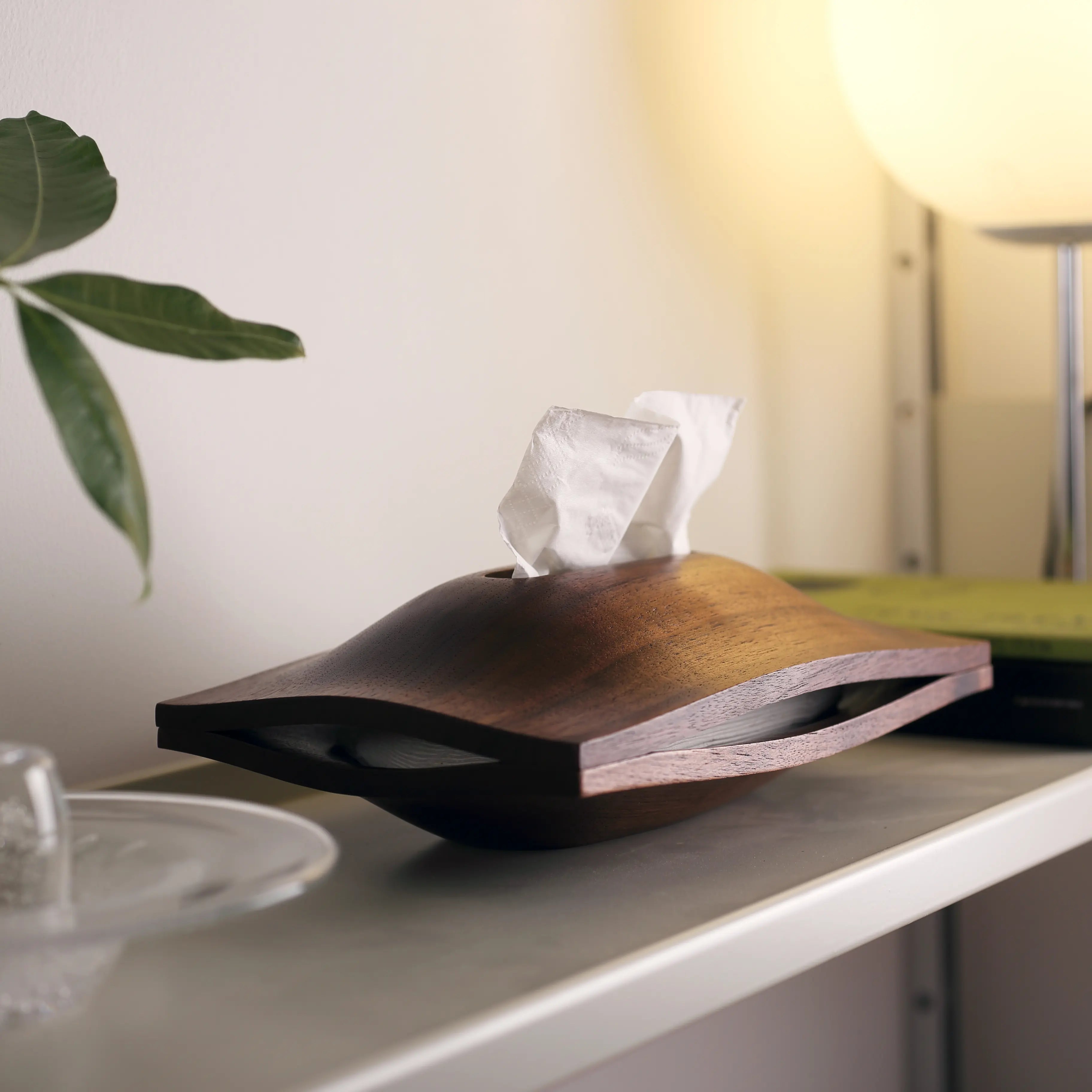 Sculptural wood tissue holder on a shelf under the warm glow of a lamp.