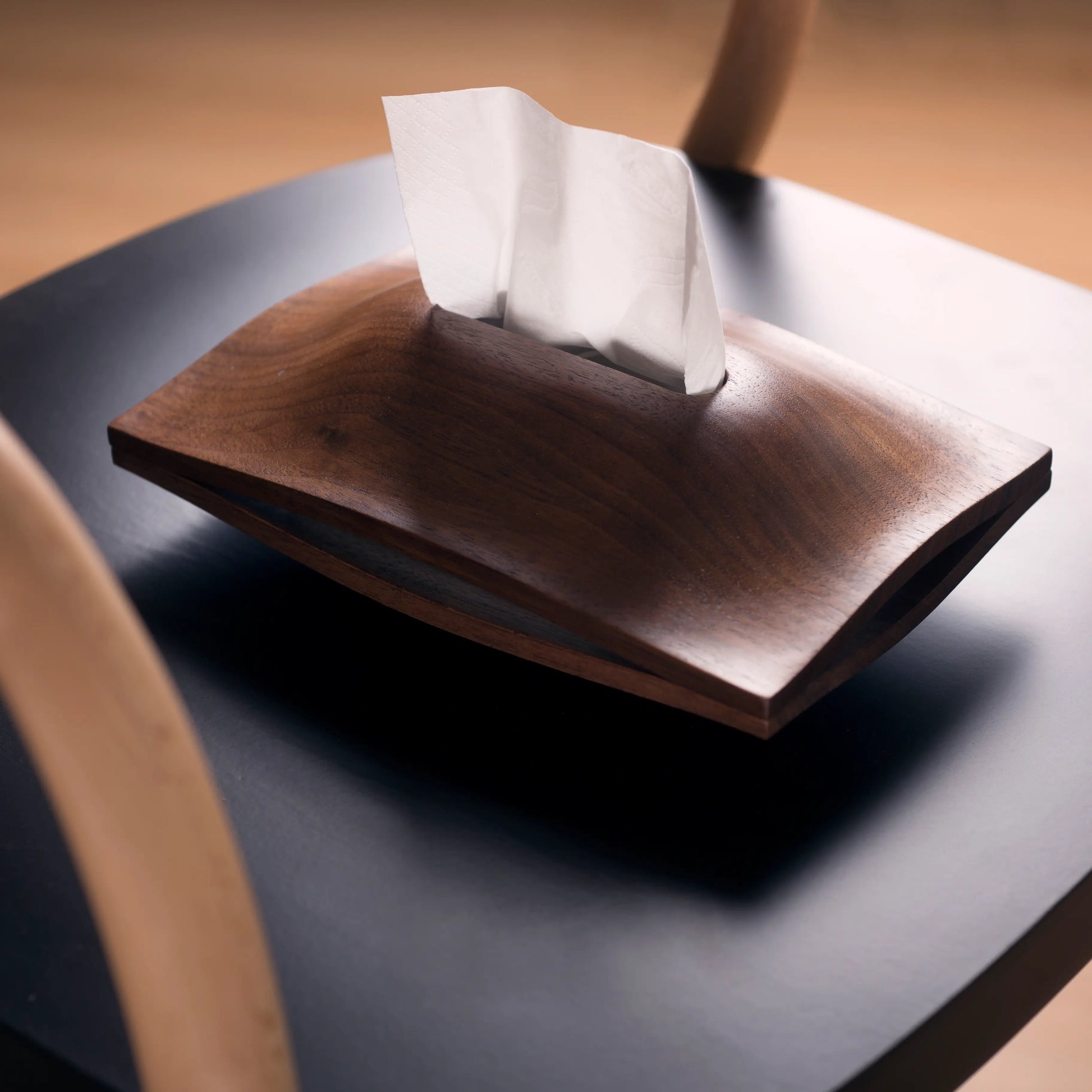 A dark wood tissue box cover sitting on a minimalist black chair.