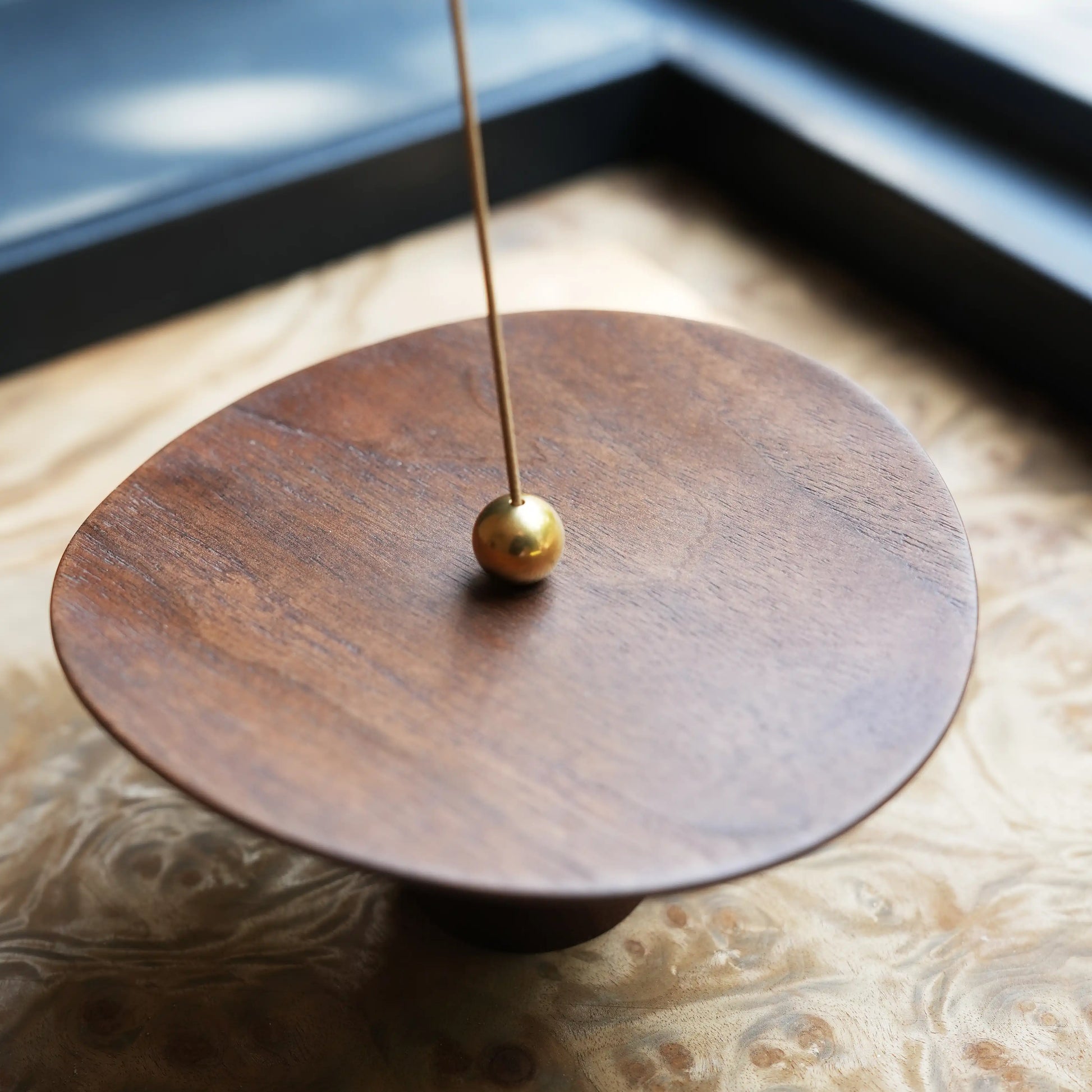 Close-up of walnut disc surface with brass ball and incense stick.