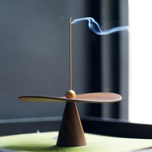 Minimalist walnut incense holder with brass ball holding a lit stick, side view.