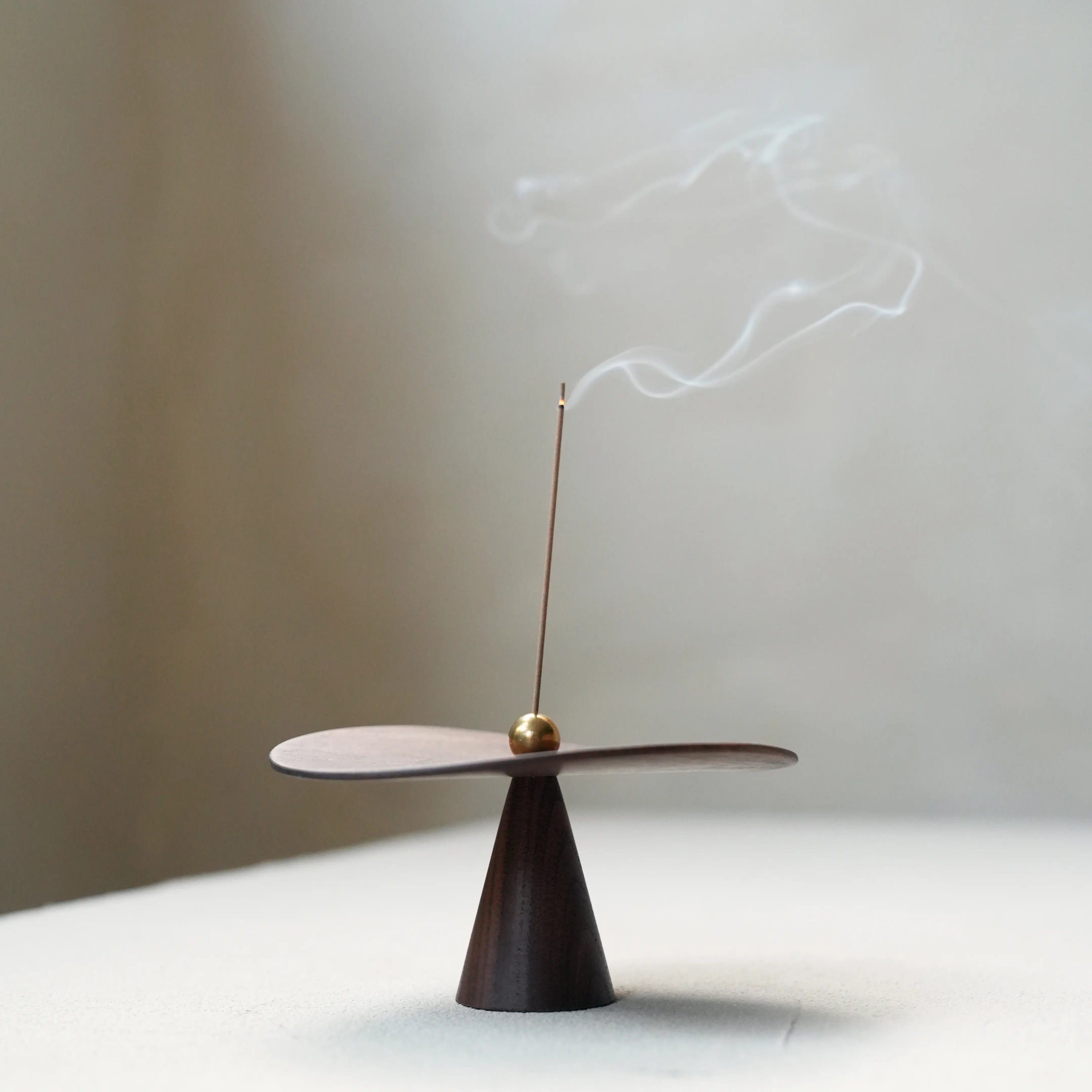Close-up of walnut disc surface with brass ball and incense stick.