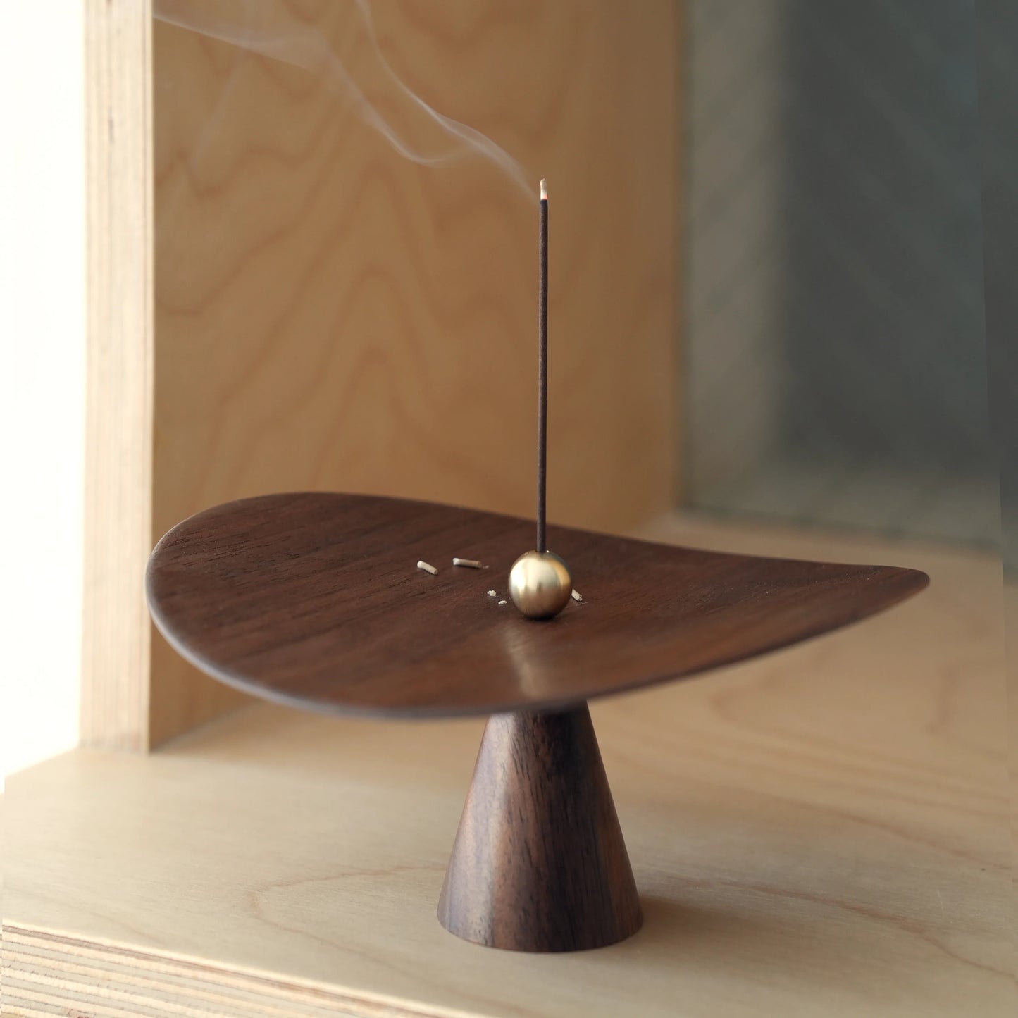 Ash fallen on the walnut dish of the sculptural incense catcher.