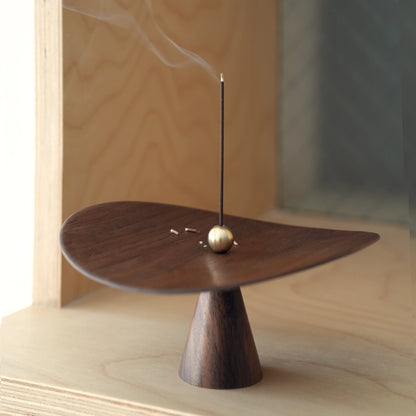 Ash fallen on the walnut dish of the sculptural incense catcher.