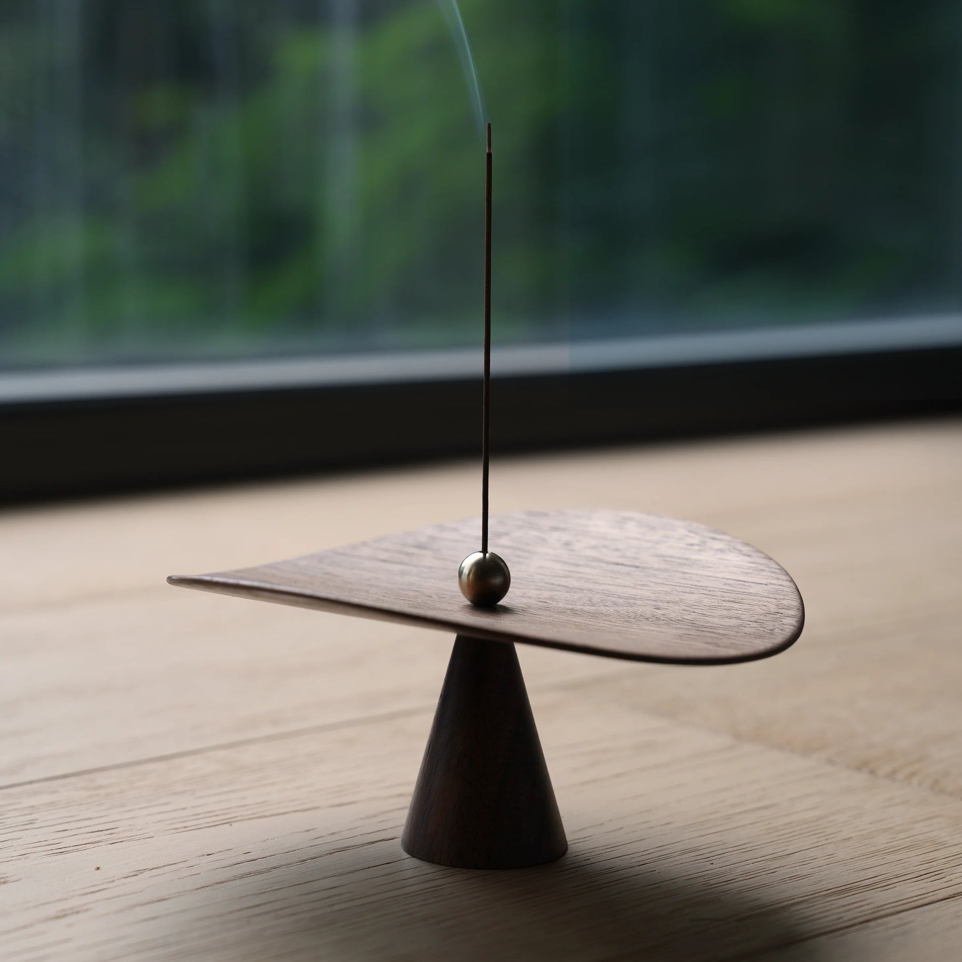 Modern walnut incense holder on a wood table with a window behind.