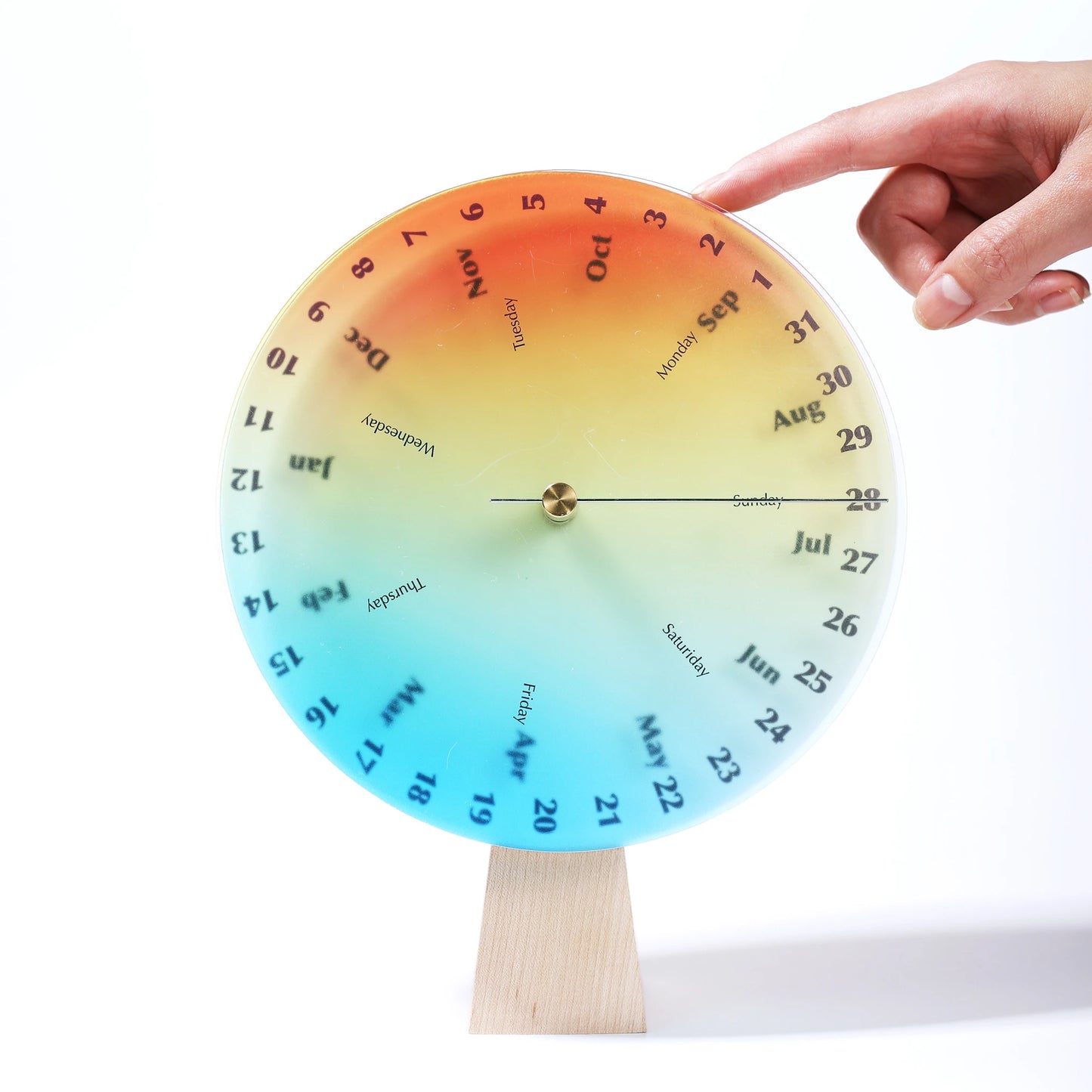 Hand turning the rainbow-colored disc of an interactive perpetual calendar.