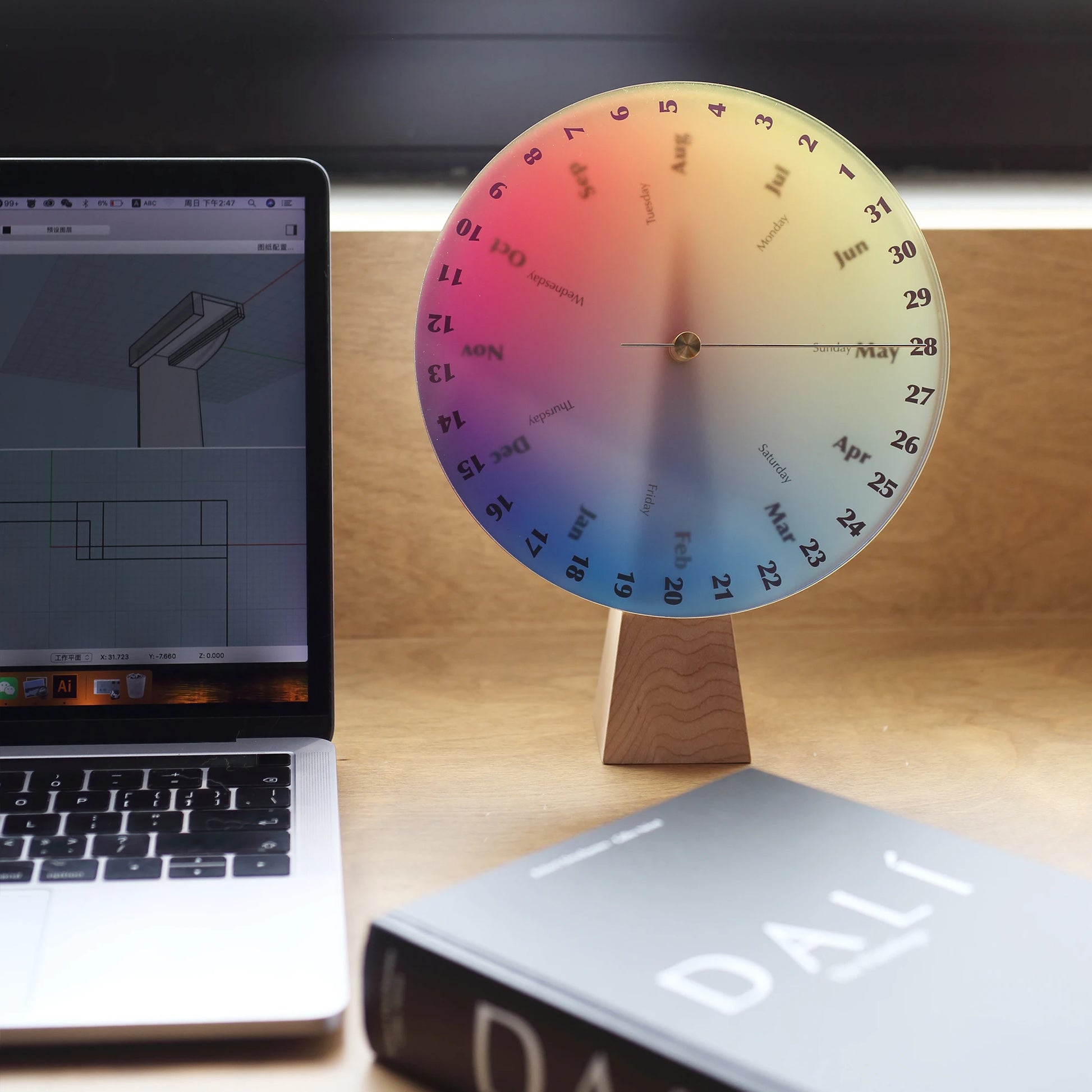 Chromatic perpetual calendar on a desk next to a laptop and book.
