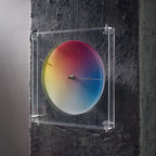 Modern color wheel clock mounted on a dark, textured concrete wall.