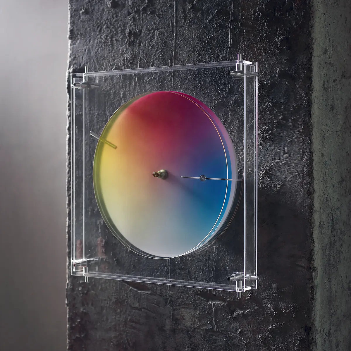 Modern color wheel clock mounted on a dark, textured concrete wall.