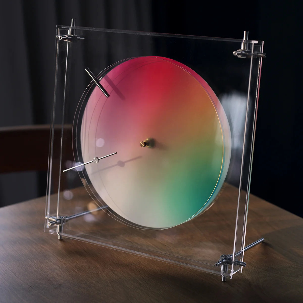 Angled view of the acrylic and metal kinetic clock on a wood table.