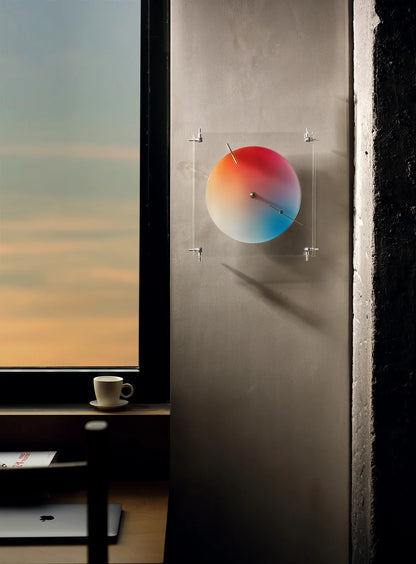 A minimalist color clock on a wall with a dramatic sunset outside.