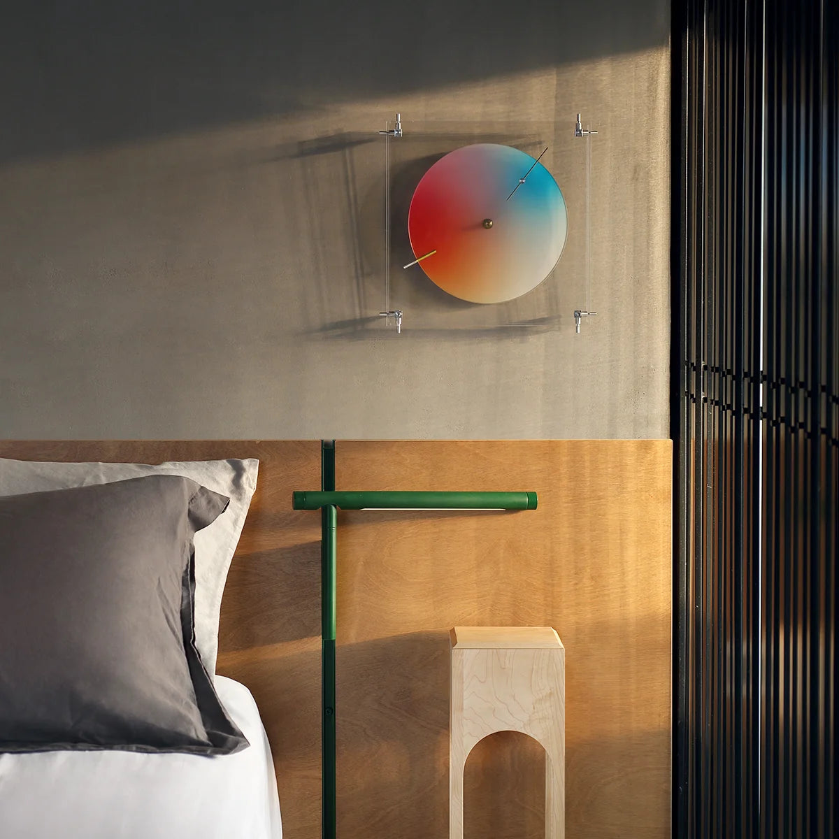 A rainbow gradient clock mounted on a wall above a modern bed.
