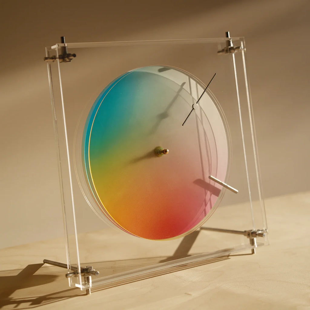 A modern acrylic clock in direct sunlight, casting colorful shadows.