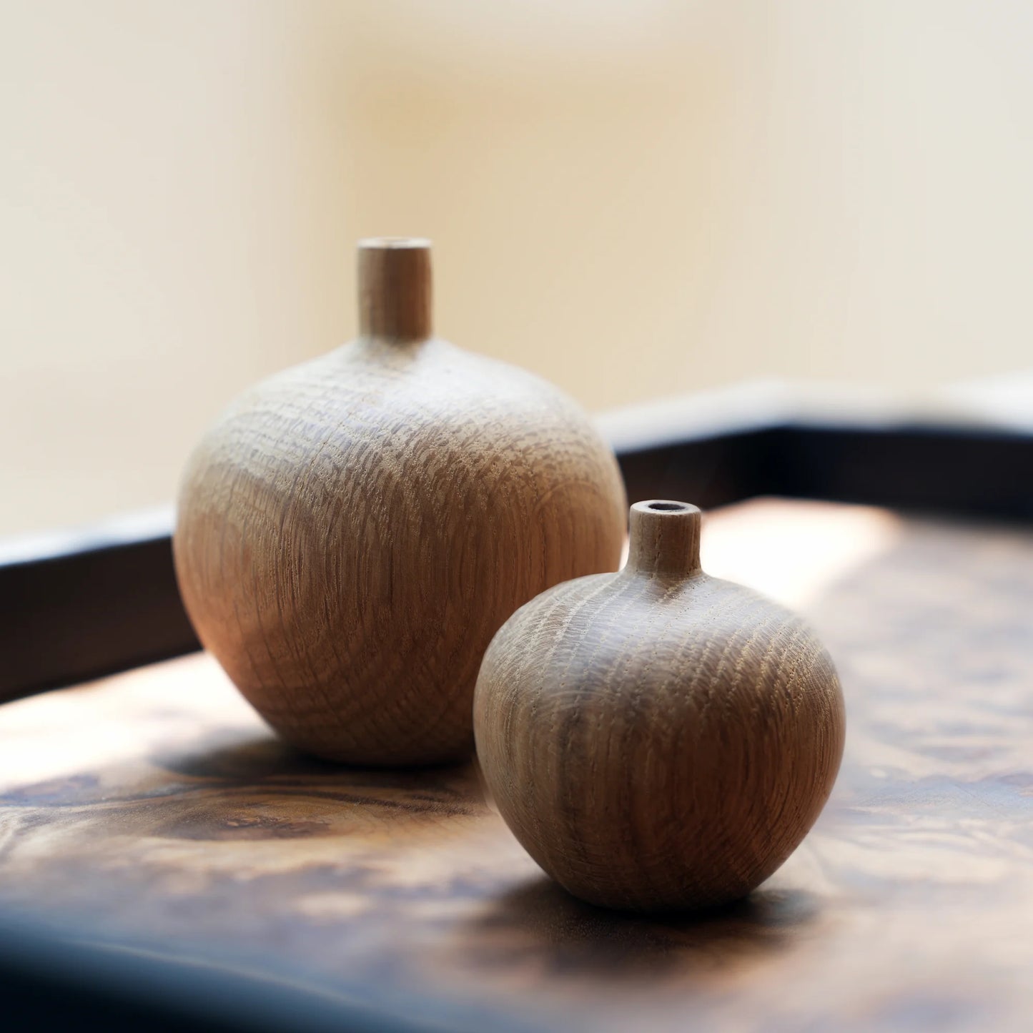 Two minimalist, spherical oak wood bud vases on a dark wood tray.