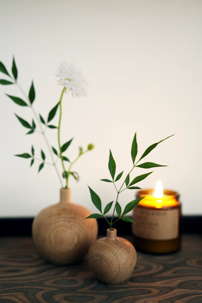 Two small oak vases holding green stems next to a lit candle.