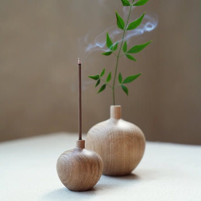 A small oak wood vase being used as a minimalist incense stick holder.