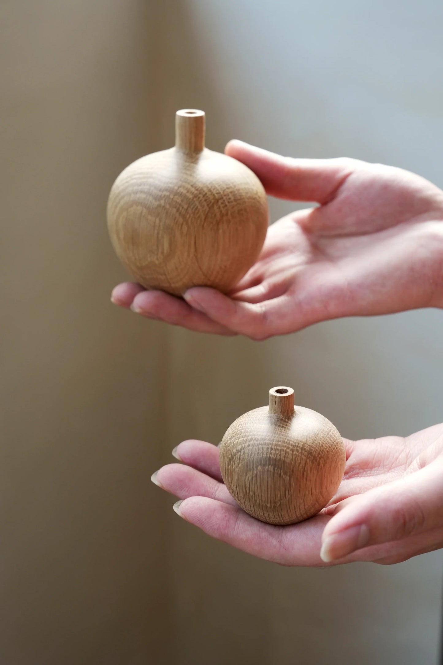 Hands holding a large and a small hand-turned oak wood bud vase.